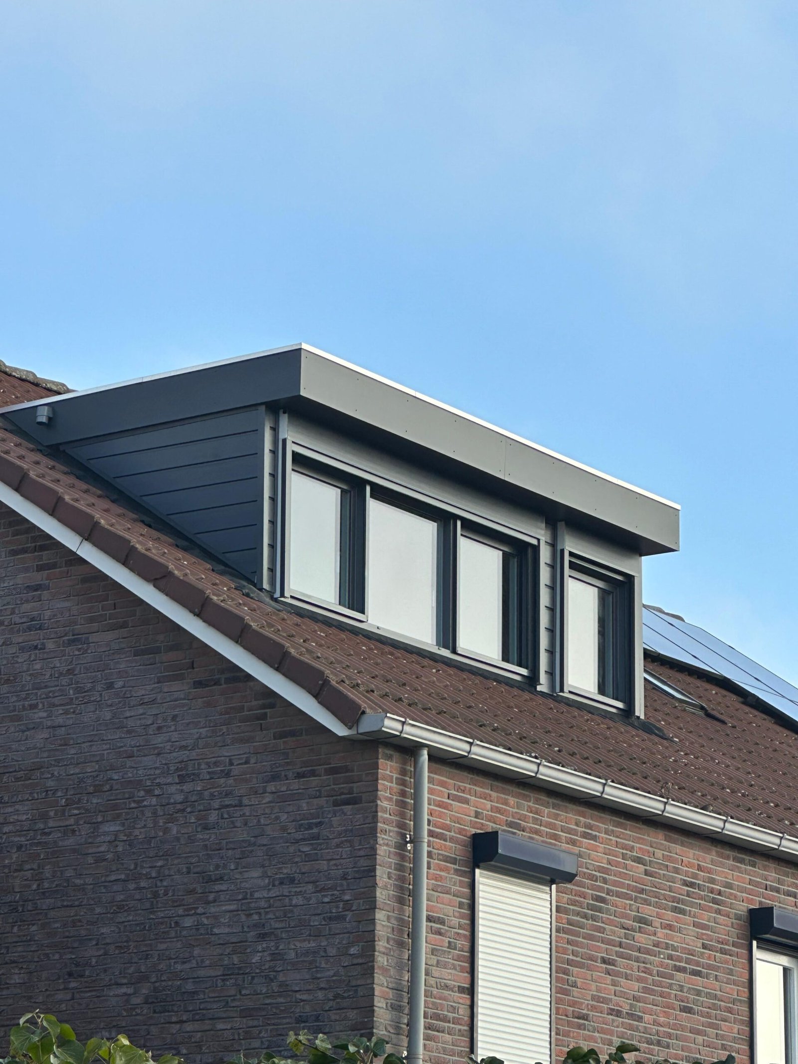 Antraciet kunststof dakkapel over de volle breedte van een bakstenen woning