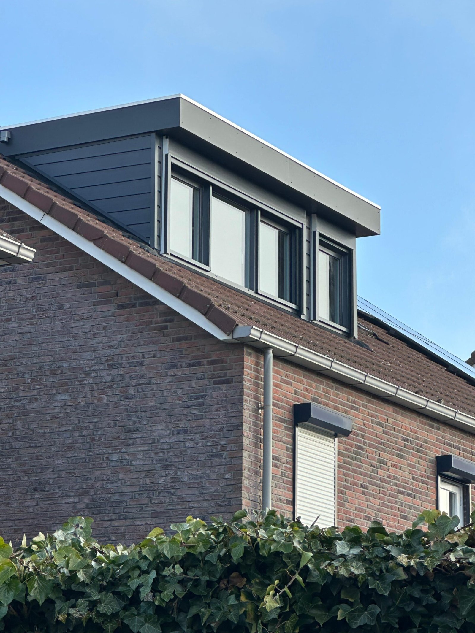 Donkere dakkapel met lichte dakrand op een bakstenen woning
