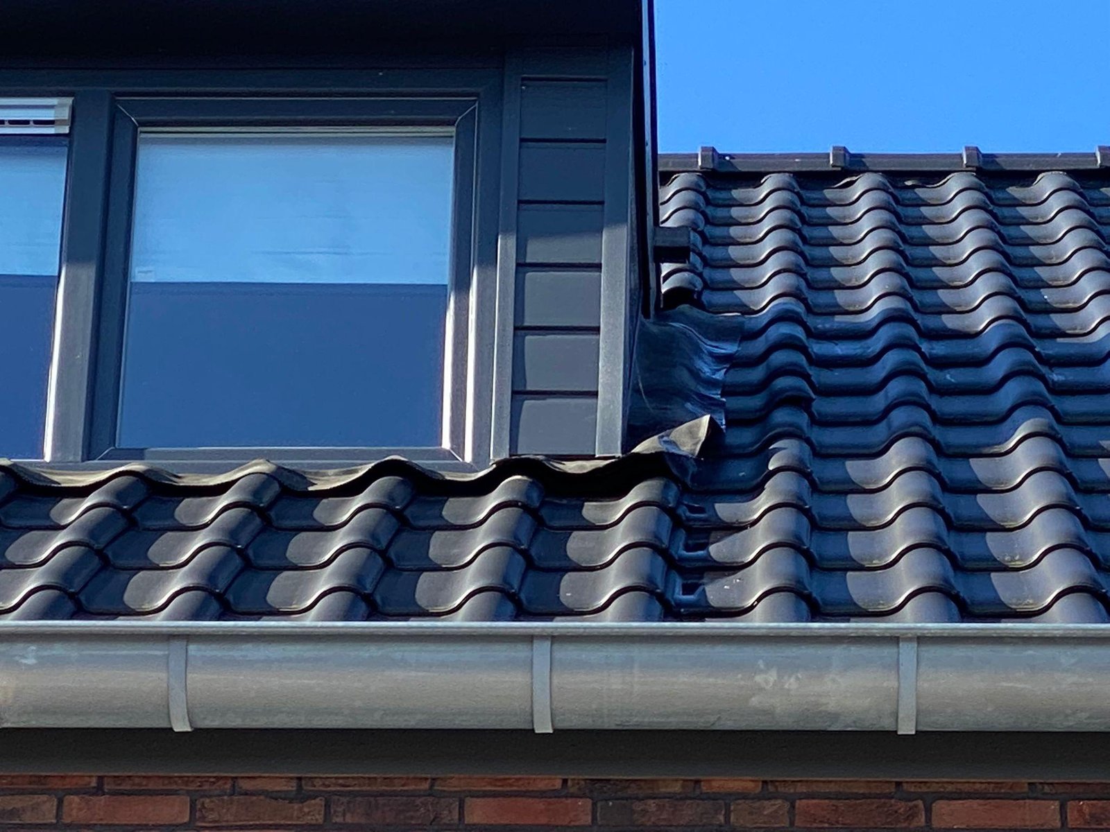 Antraciet dakkapel met vier raamdelen tegen een blauwe lucht